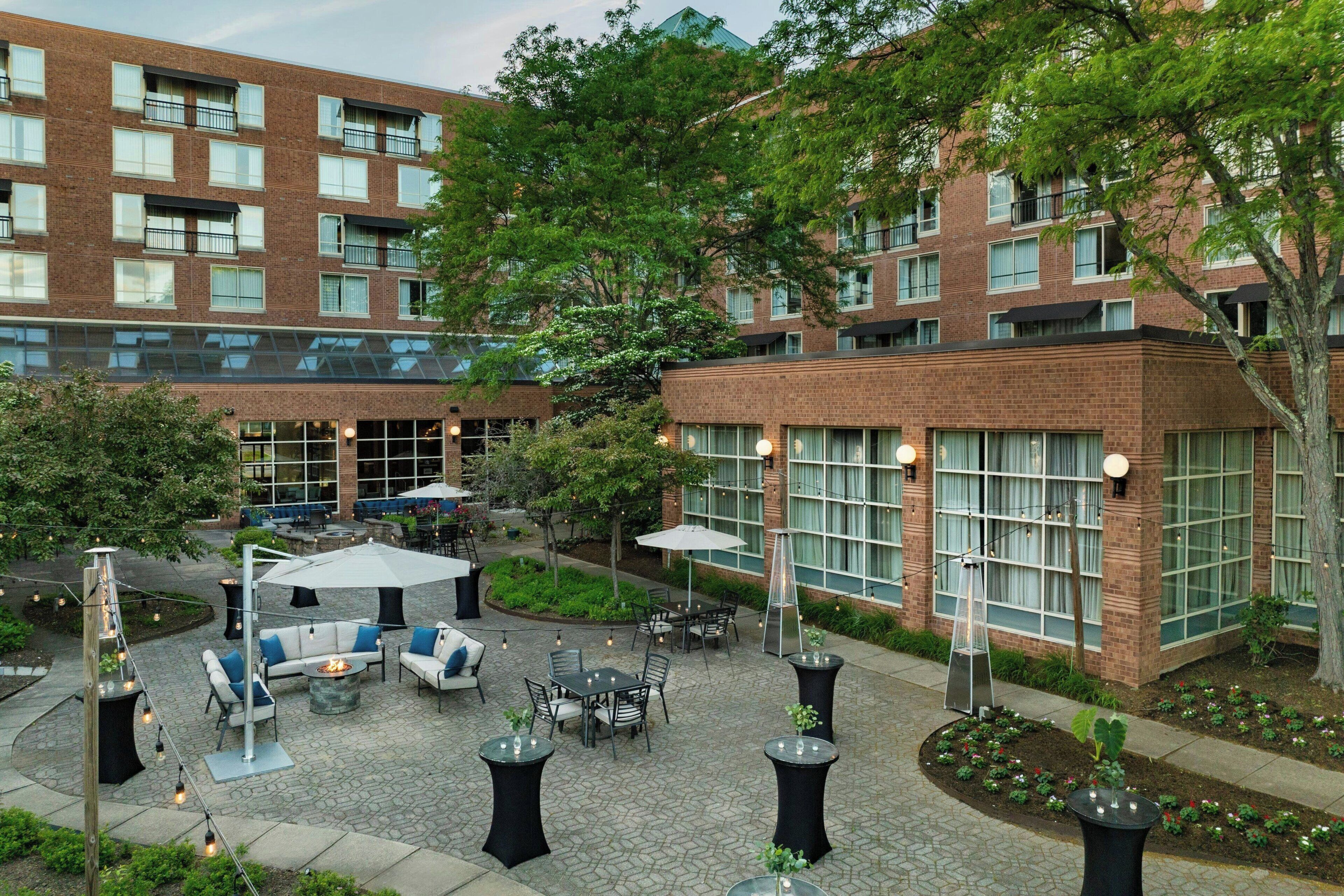 Un patio con mesas al aire libre, un edificio de ladrillo y un árbol.