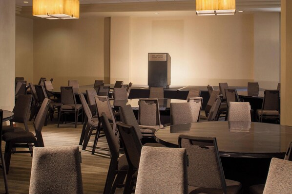 Un salón de conferencias con varias mesas y sillas, un atril e iluminación en el techo.