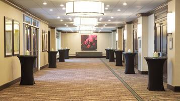 A hotel corridor with a carpeted floor, black tables with candles, and a large floral painting on the wall.
