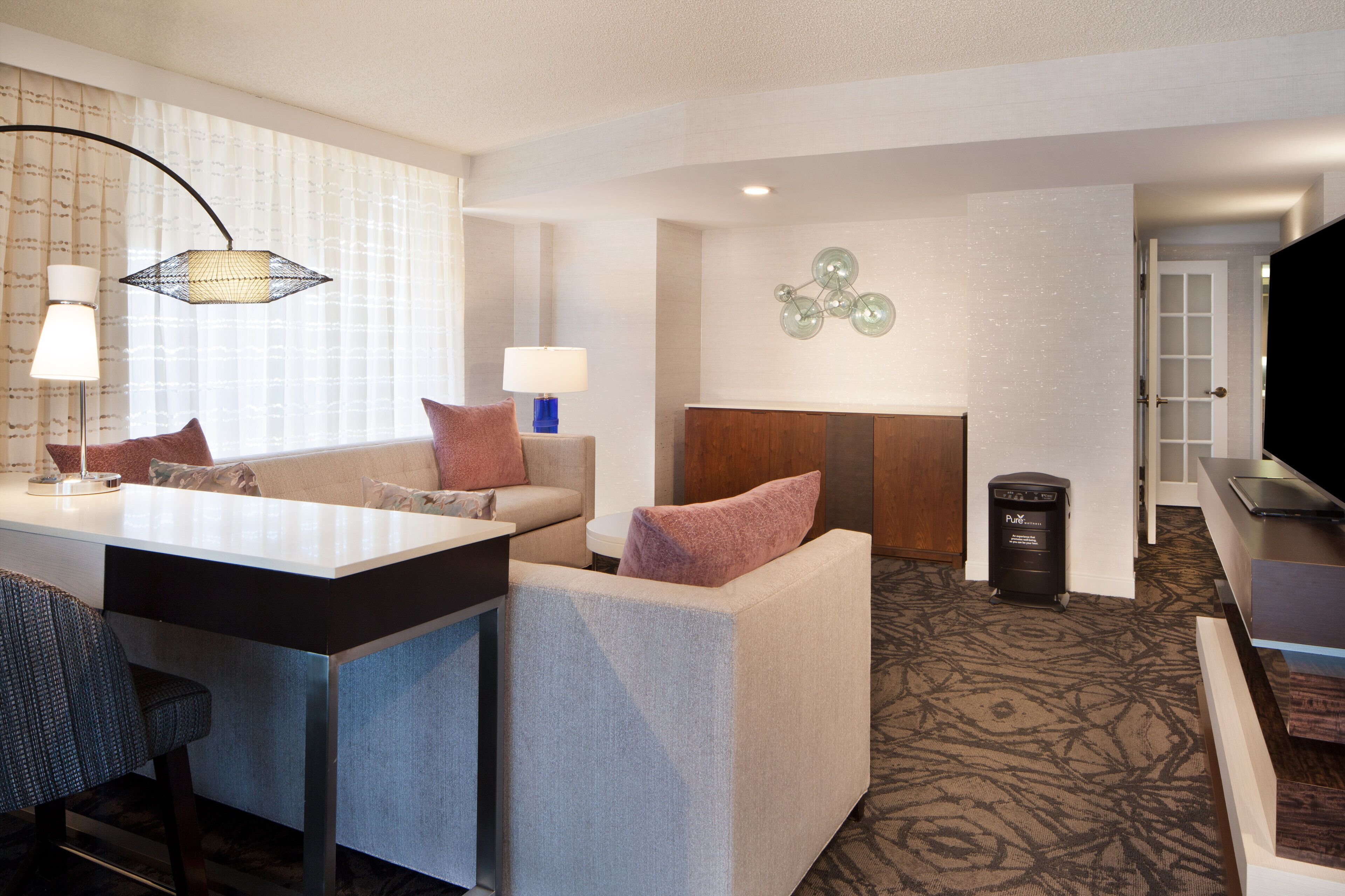 A hotel room with a sofa, a small table, a lamp, a TV, and a trash bin.