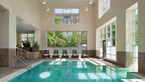 A large indoor swimming pool with clear glass walls, multiple windows, and a seating area with chairs and a small staircase. - The Westin Princeton at Forrestal Village (Princeton)