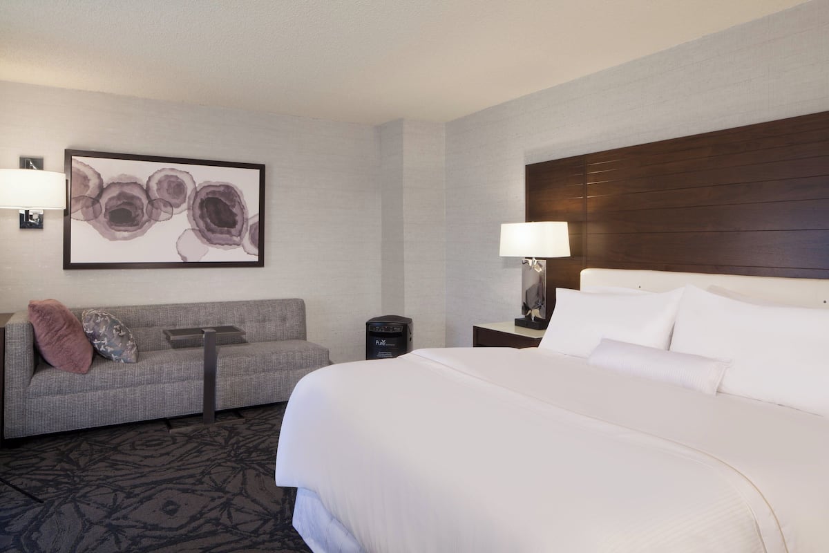 A hotel room with a large bed, a sofa, a wall-mounted artwork, a lamp, and a small table.