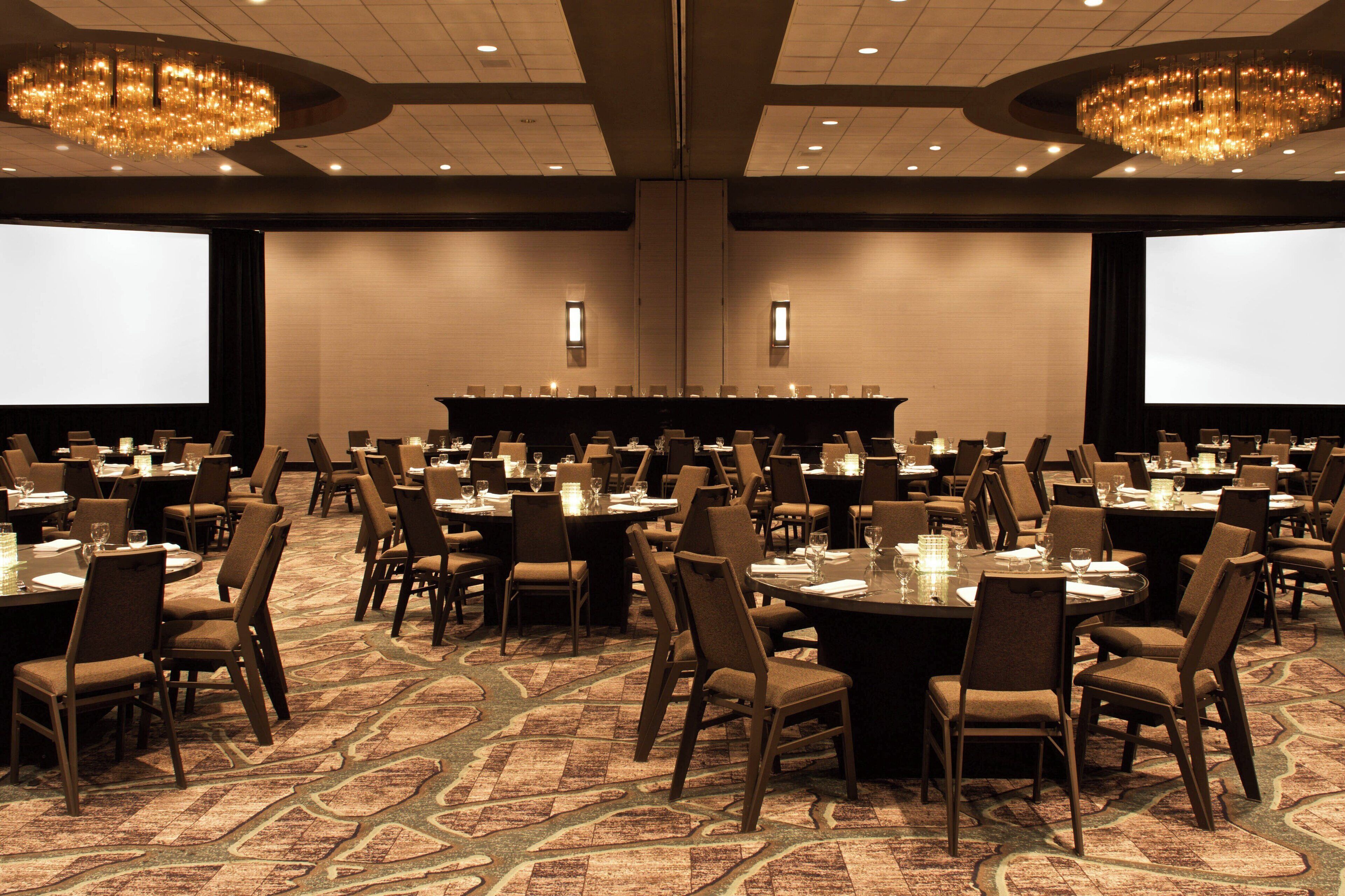 A conference room with multiple tables and chairs, large screens, and chandeliers.