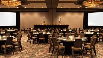 A conference room with multiple tables and chairs, large screens, and chandeliers.