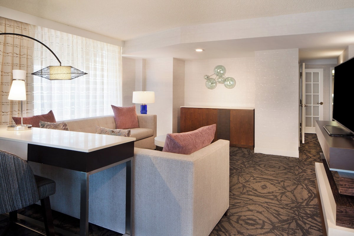 A hotel room with a sofa, a small table, a lamp, a television, and a decorative wall piece.