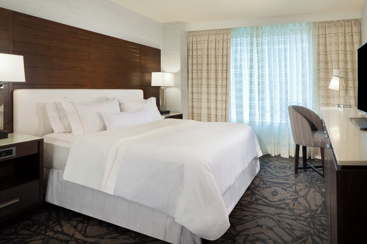 A hotel room with a large bed, a desk with a chair, a television, and a window with curtains.
