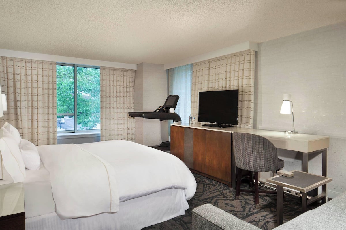A hotel room with a bed, a desk with a chair, a television, and a lamp.
