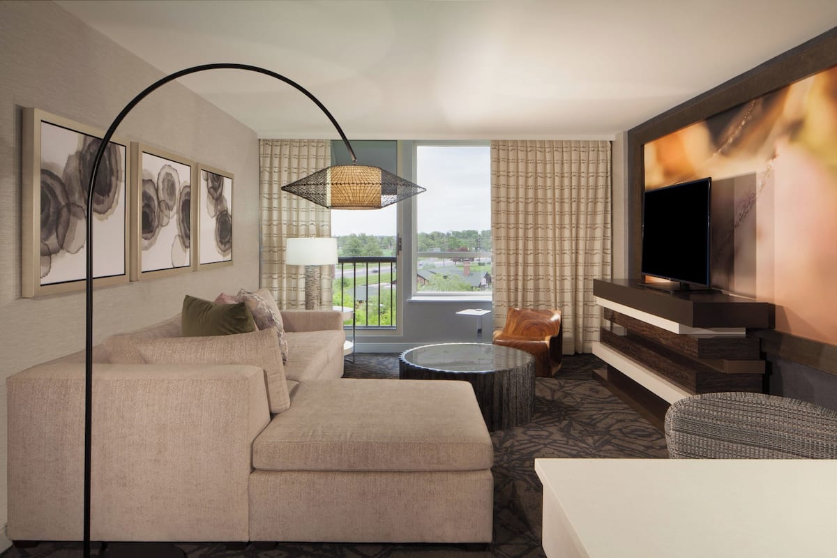 A modern hotel room with a sofa, a TV, a balcony with a view, and artwork on the wall.