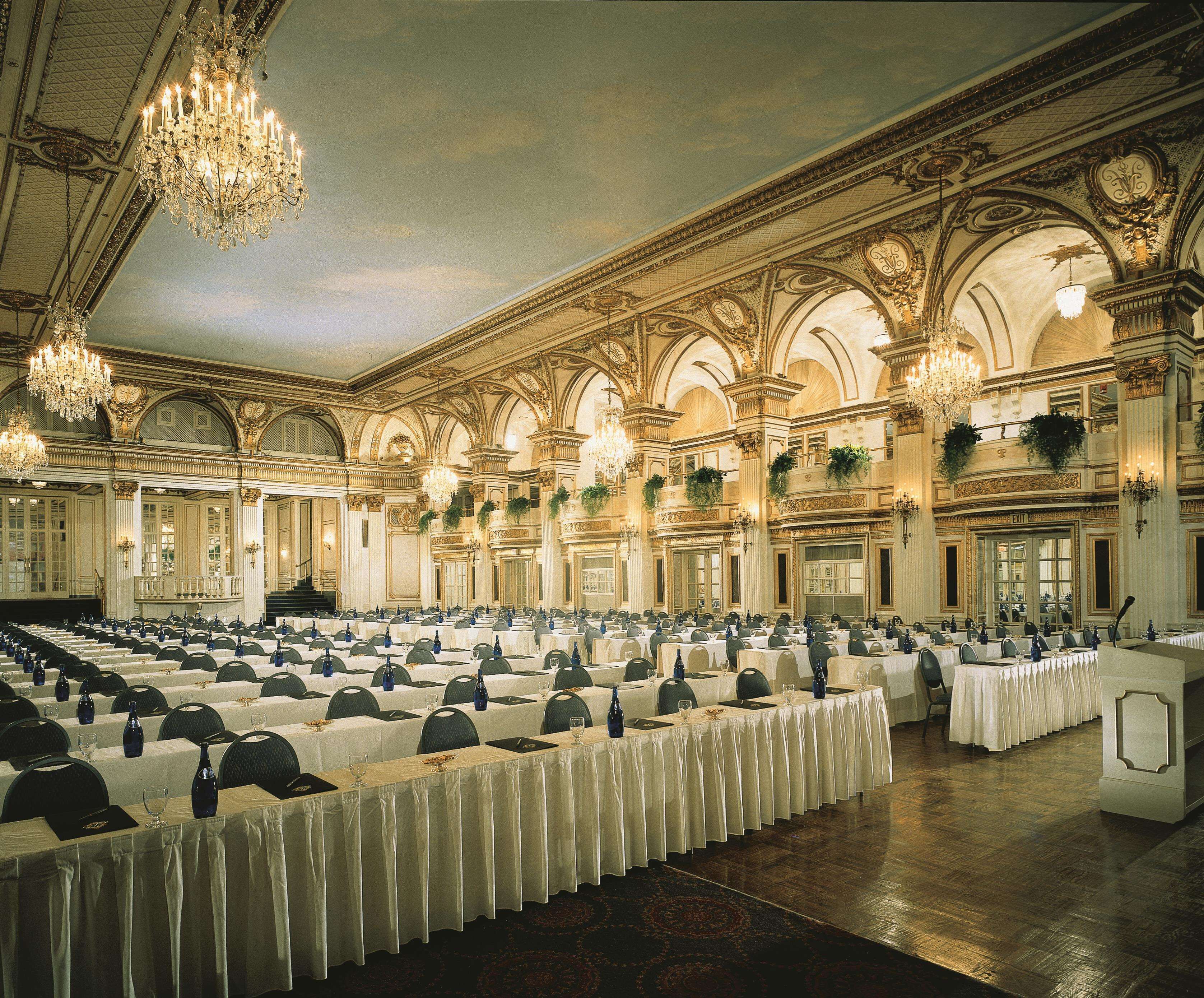 A grand banquet hall with ornate chandeliers, high ceilings, and a long table set for a formal event.