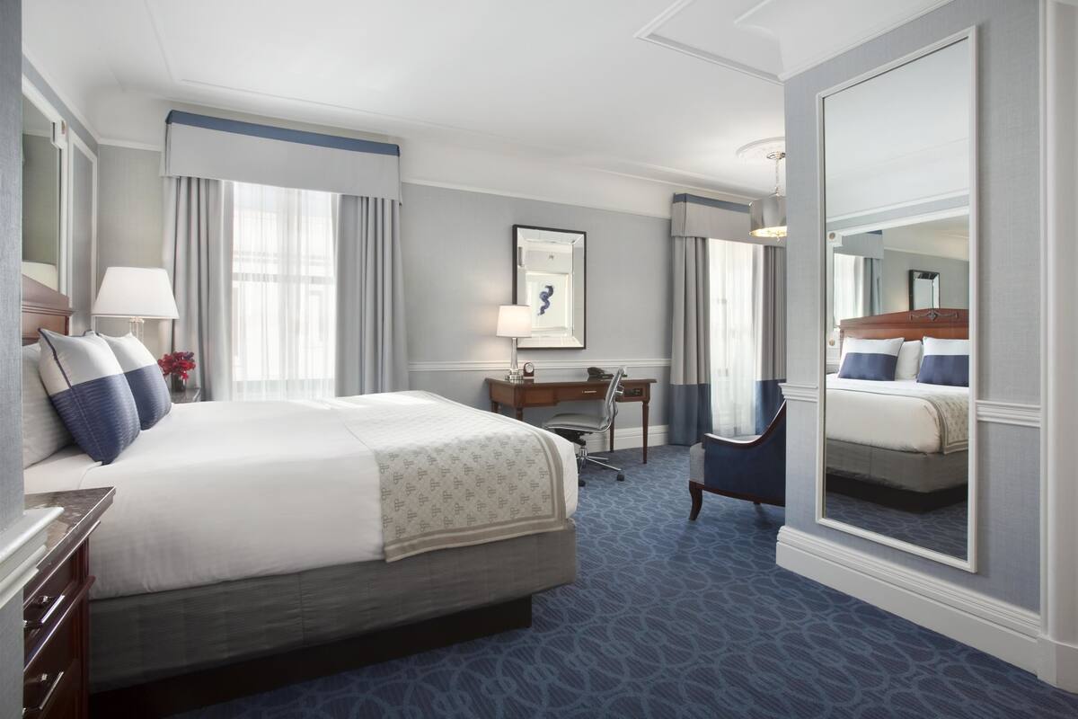 A hotel room with a large bed, a desk, a chair, and a mirror.