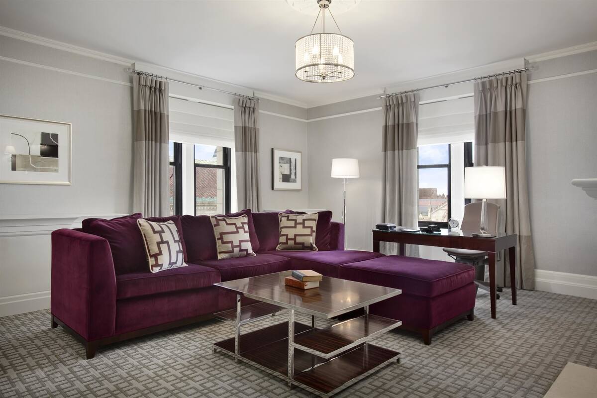 A modern living room with a purple sectional sofa, a glass coffee table, and a desk with a lamp.