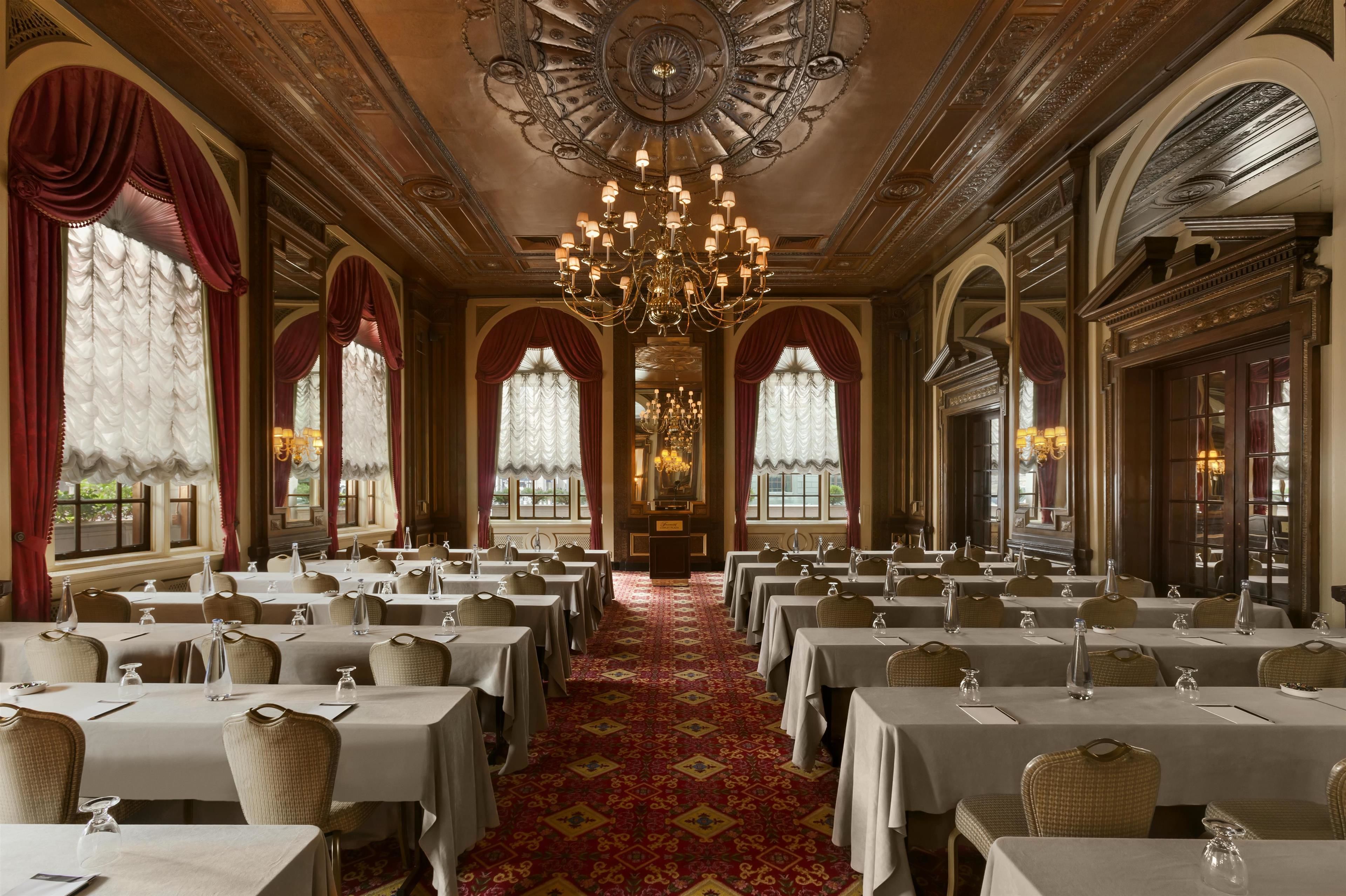 A formal dining room with multiple tables, chandeliers, and ornate ceiling details.