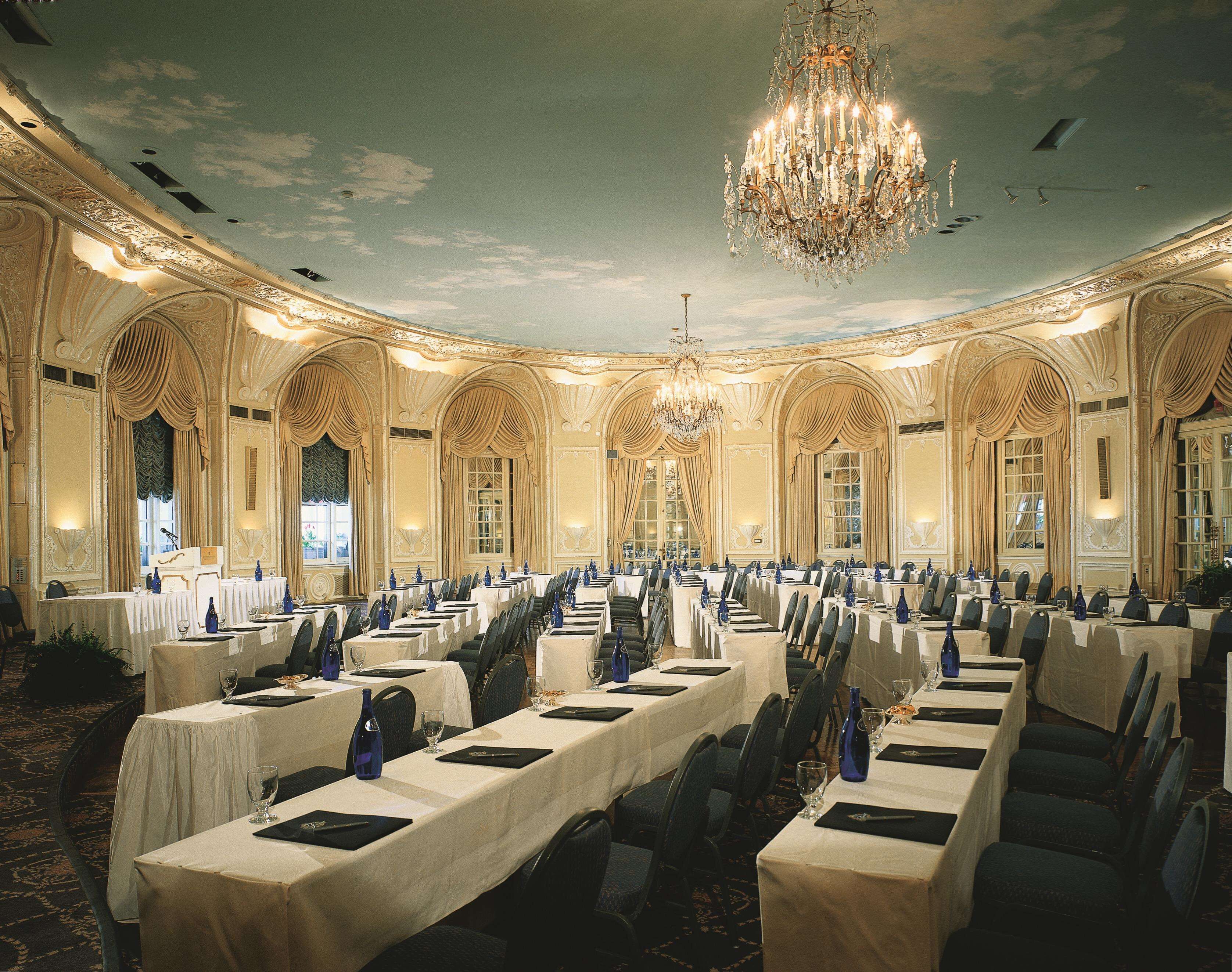 A banquet hall with long tables set for a formal event, ornate ceiling, and chandeliers.