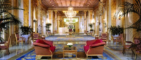 A grand lobby with a chandelier, red upholstered chairs, and a patterned carpet.