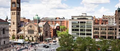 A historic building with a prominent tower, surrounded by modern buildings and a busy street with pedestrians and vehicles.