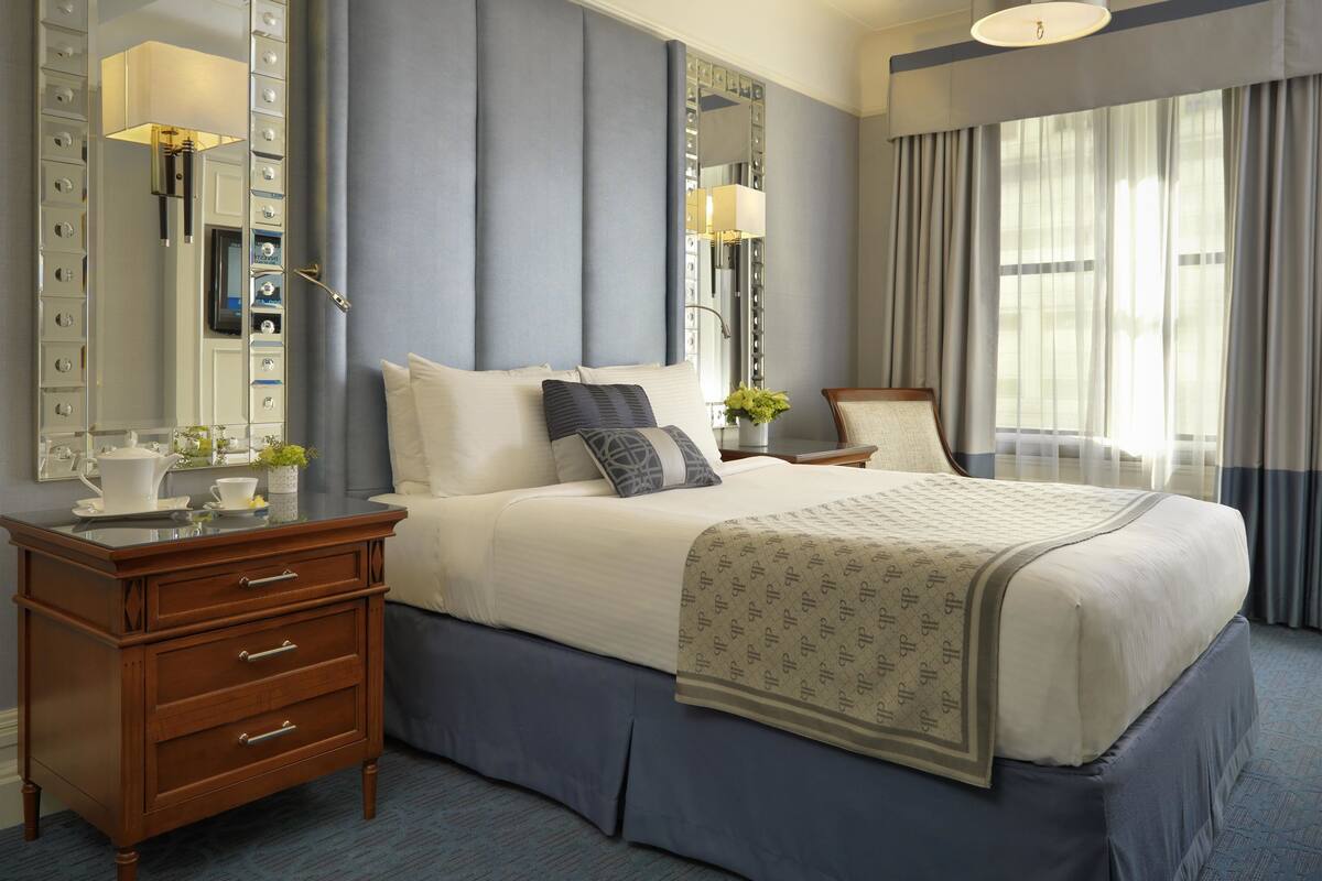 A hotel room with a large bed, a wooden dresser, a bedside table with a lamp, and a large mirror.