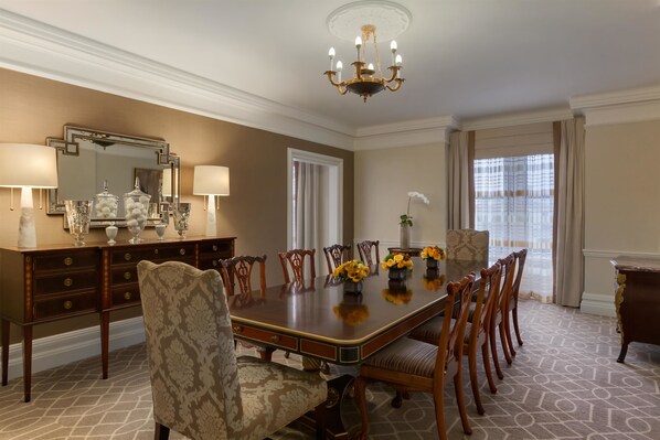 A formal dining room with a long table, chairs, a chandelier, and a large mirror.