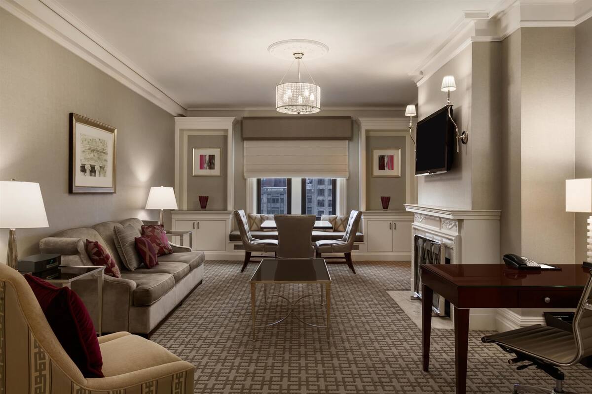 A hotel room with a sofa, armchair, dining table, and a fireplace.