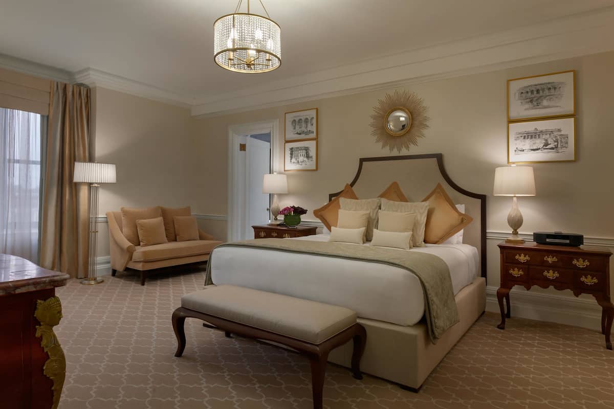 A hotel room with a large bed, a bench, a sofa, and two nightstands.