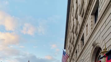 Eine Theaterwerbetafel mit der Aufschrift "The Fairmont Copley Plaza", eine große amerikanische Flagge und ein historisches Gebäude mit einem Uhrturm im Hintergrund.