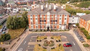 Un grand bâtiment portant les enseignes « Royal Victoria » et « Crowne Plaza », entouré d’une place aménagée avec une fontaine, un parking et une route où la vitesse est limitée à 5 miles par heure.