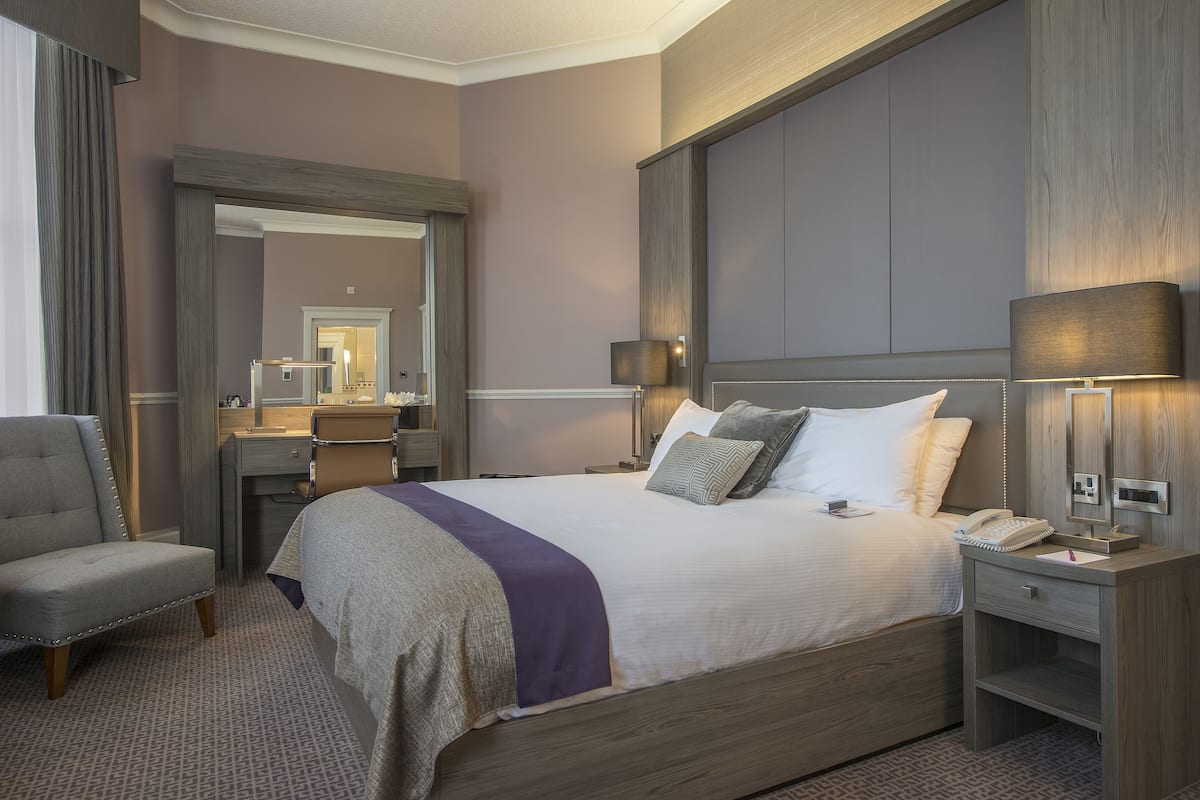 A hotel room with a large bed, bedside lamps, a desk, and a chair.