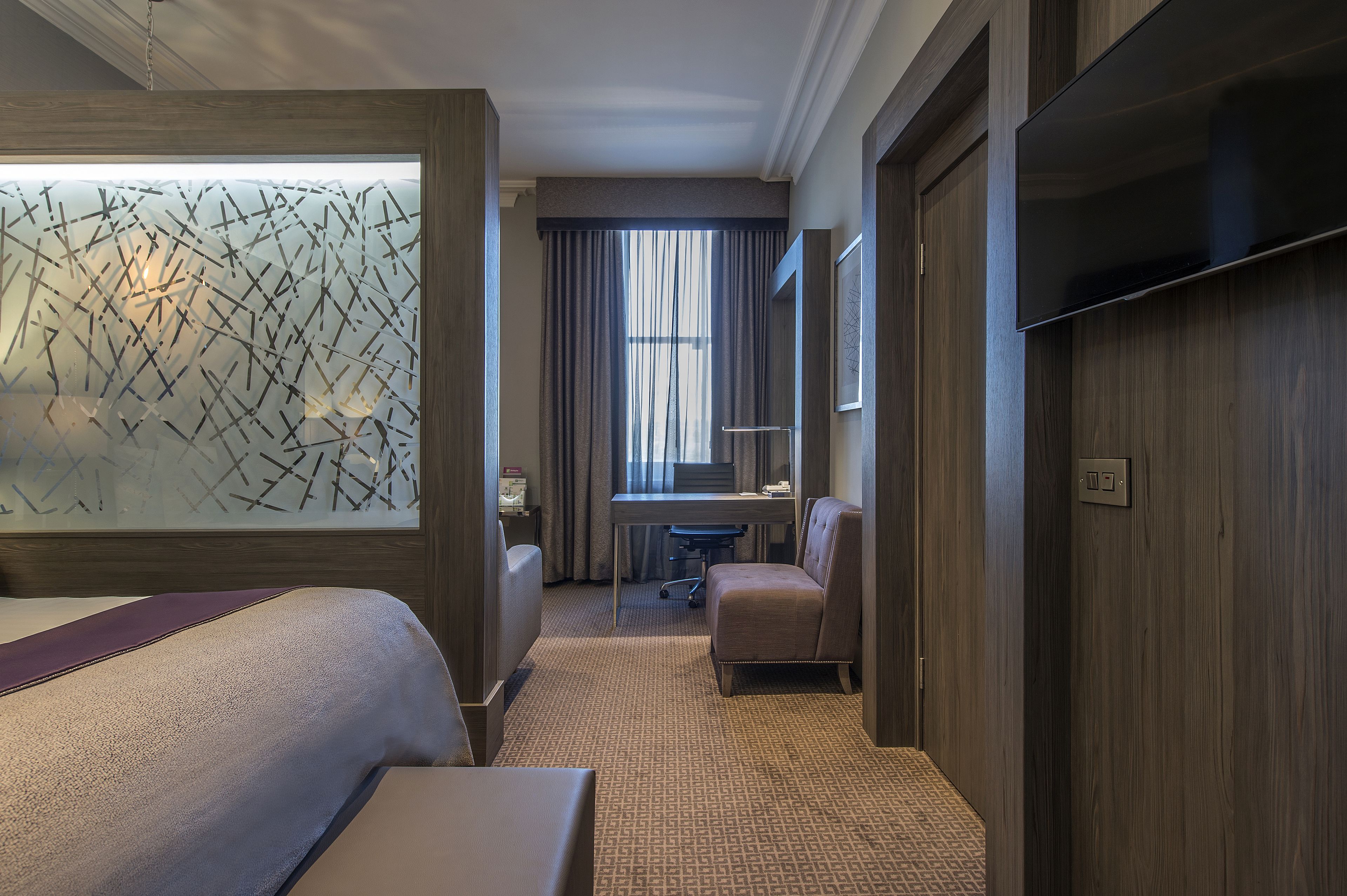 Quarto de hotel com uma cama grande, escrivaninha, cadeira e televisão na parede.