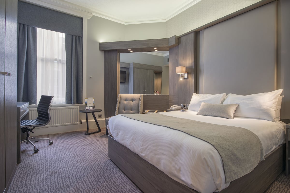 A hotel room with a large bed, a desk, and a chair.