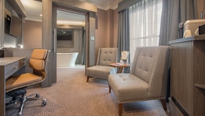 Une chambre d’hôtel équipée d’un bureau, de deux fauteuils, d’une petite table, d’une télévision et d’une baignoire.