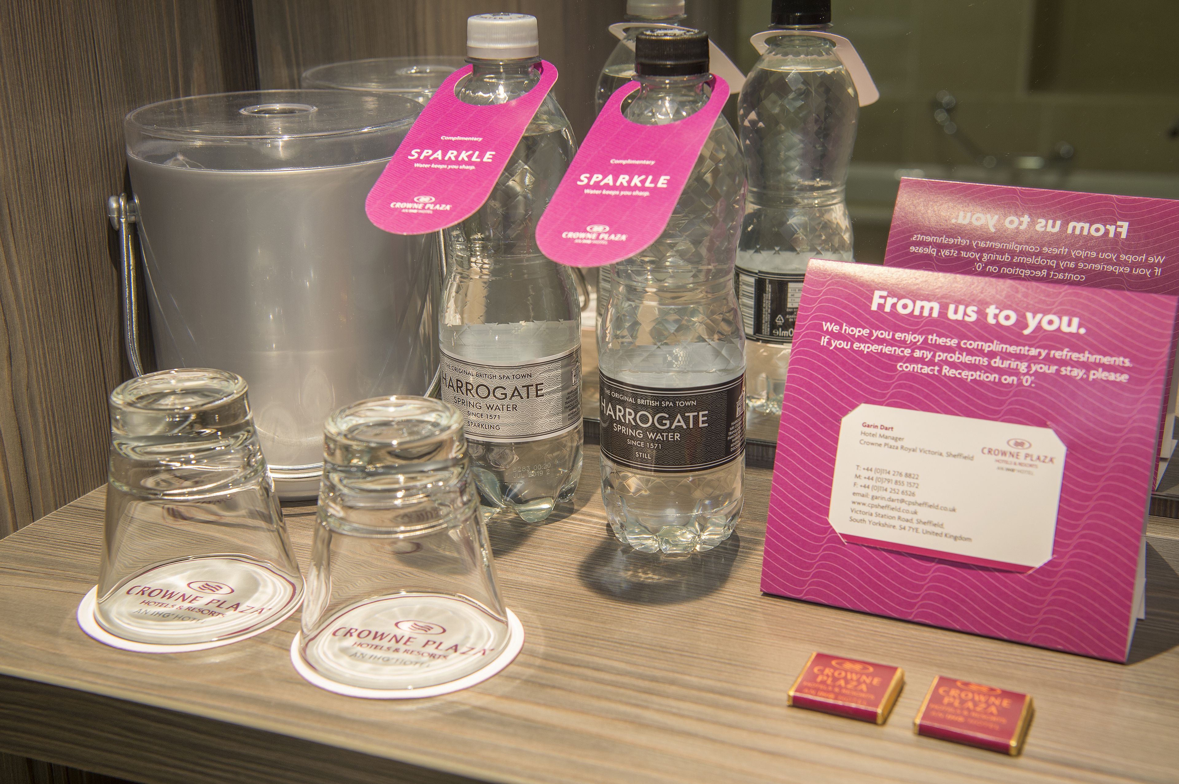 A display of water bottles and glasses with labels, a sign with contact information, and a wooden surface.