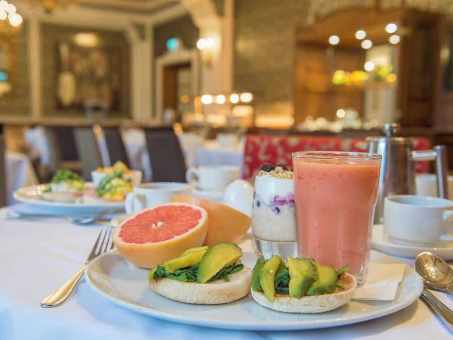 A breakfast setting with a plate of toast topped with avocado and greens, a grapefruit, and a glass of smoothie.