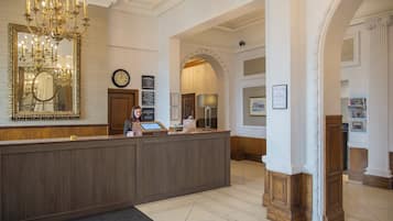 A reception area with a wooden reception desk, a large mirror, a chandelier, and a clock on the wall.