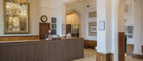 A reception area with a wooden reception desk, a large mirror, a chandelier, and a clock on the wall.