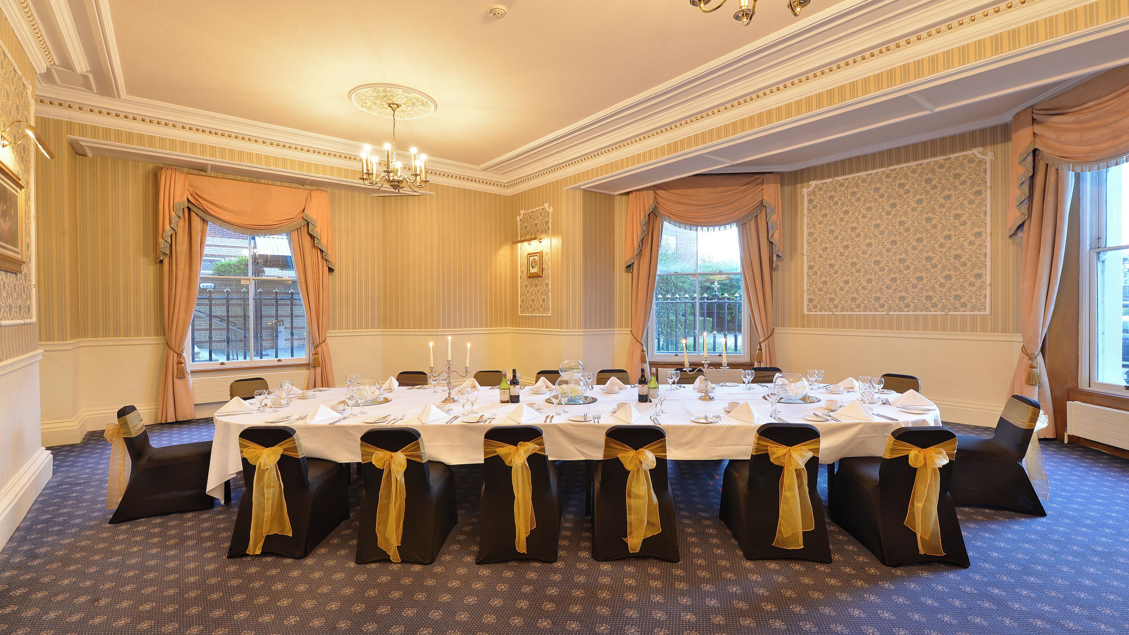 A formal dining room with a long table set for a meal, elegant chairs, and a chandelier.