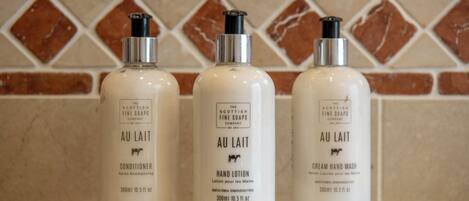 Three bottles of 'Au Lait' hand lotion on a clear shelf against a tiled wall.