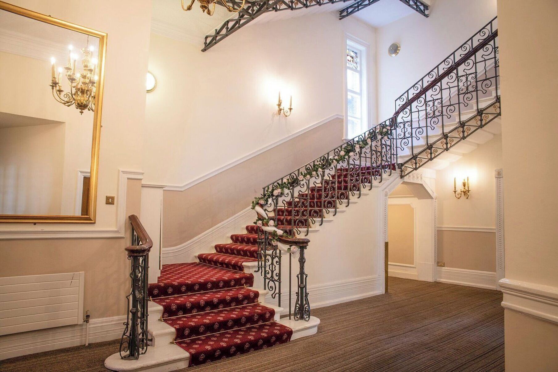 A grand staircase with red carpeted steps, ornate metal railings, and a chandelier.