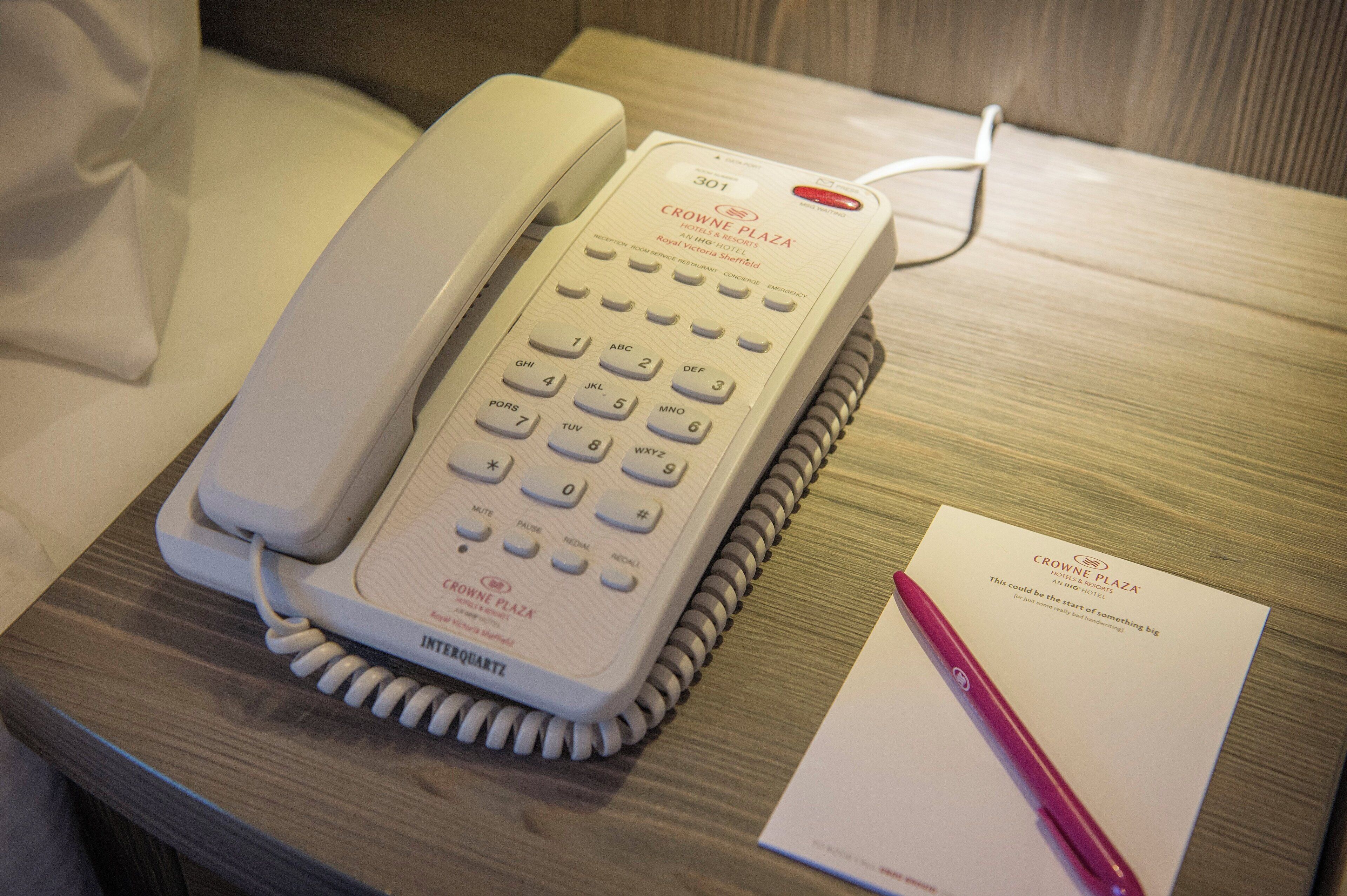 Una habitación de hotel con un teléfono en la mesita de noche, un bloc de notas y un bolígrafo sobre una mesita de madera.