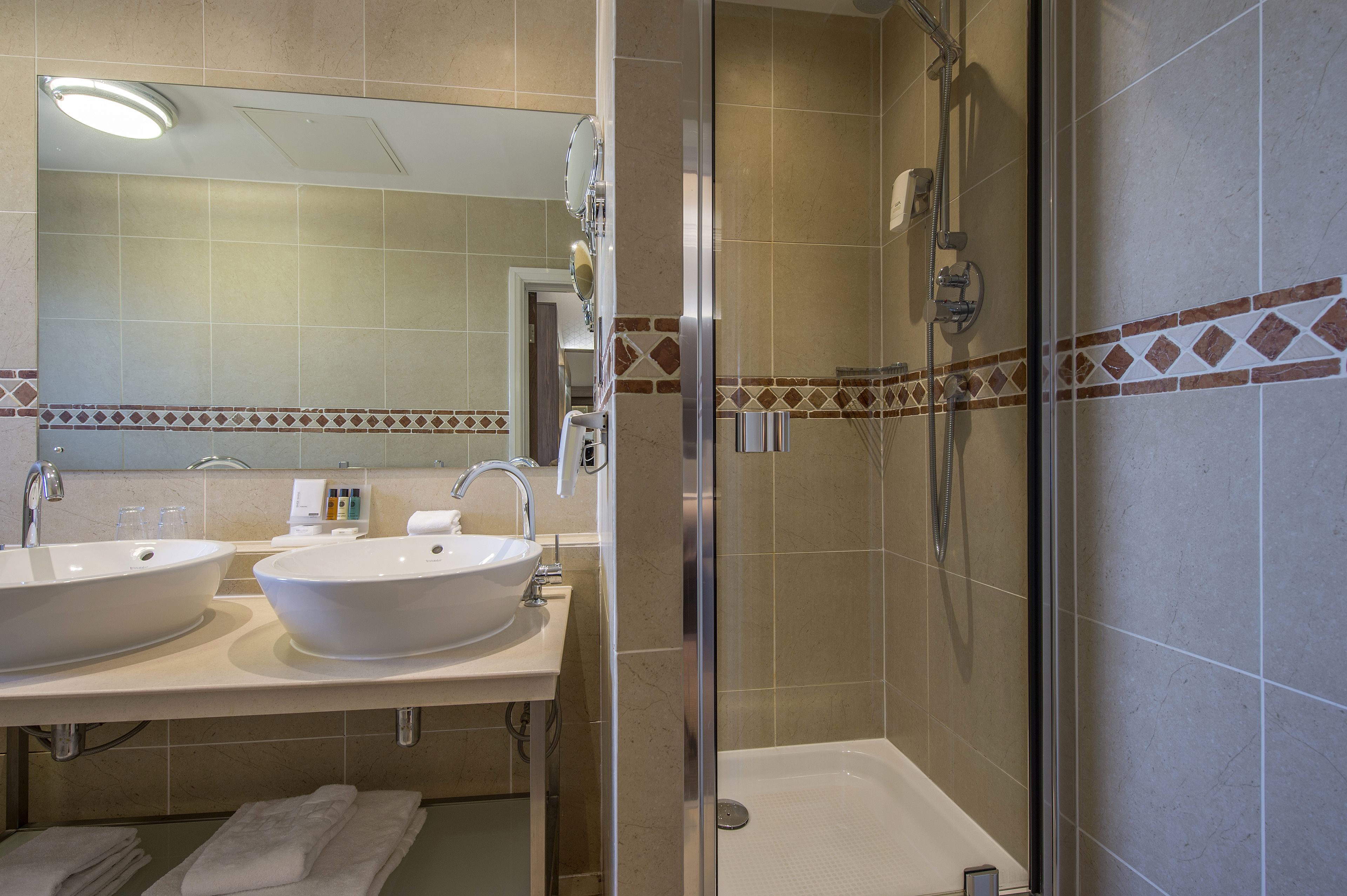 A bathroom with two sinks, a shower, and a glass-enclosed shower area.