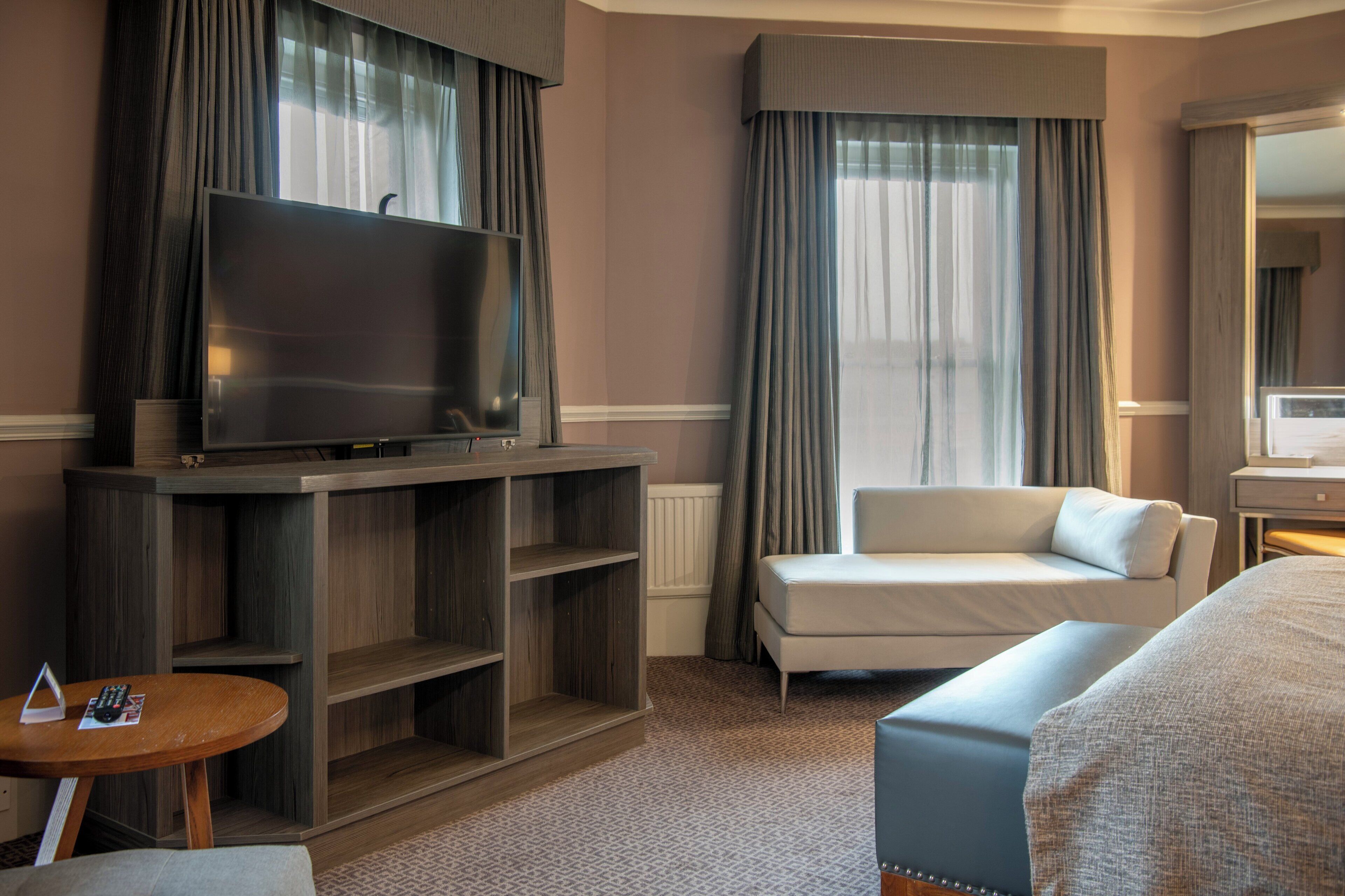 A hotel room with a large flat-screen TV, a sofa, a bed, and a small table.