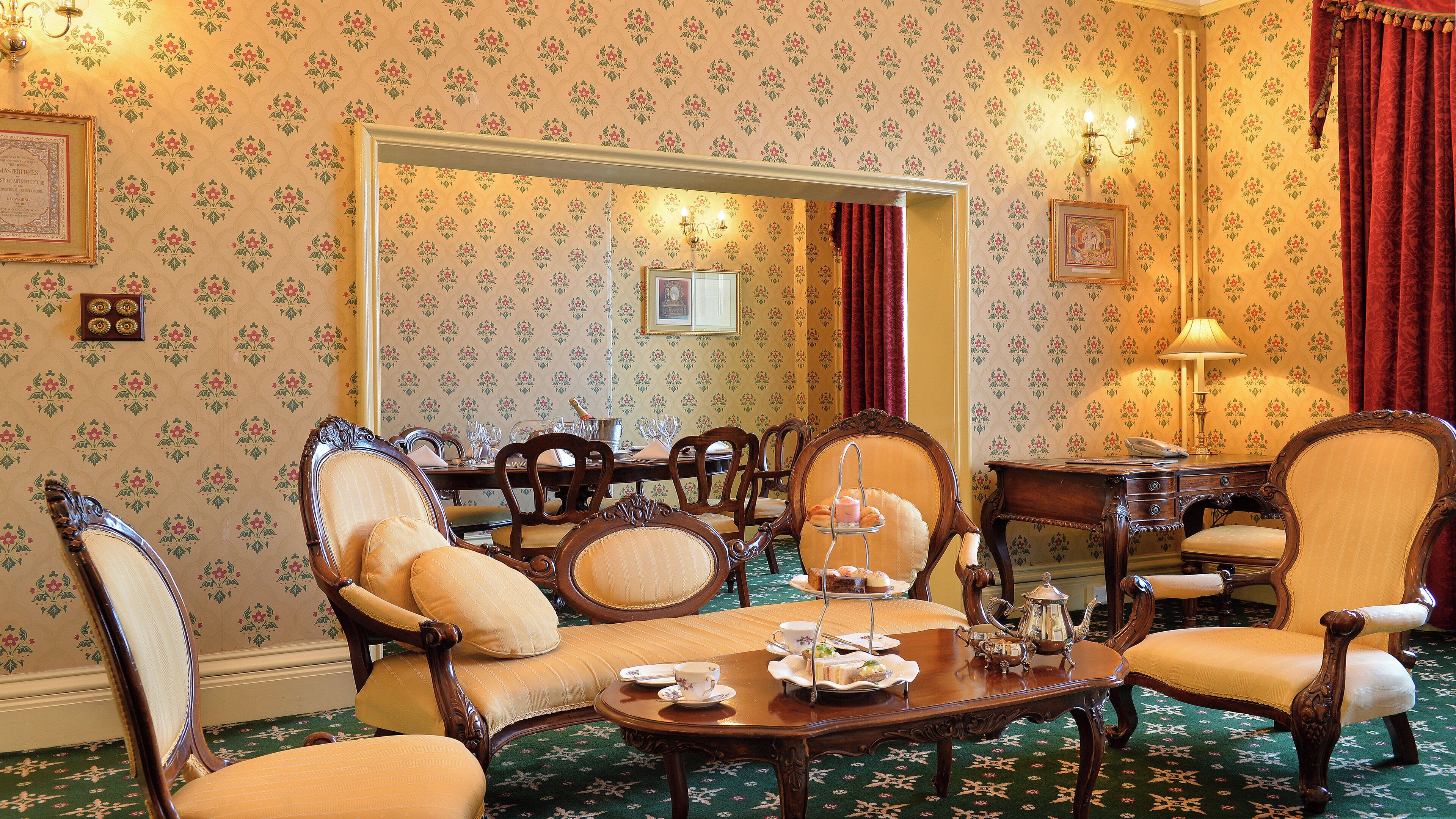 A room with a dining table set for four, surrounded by ornate chairs, a mirror, and a lamp.