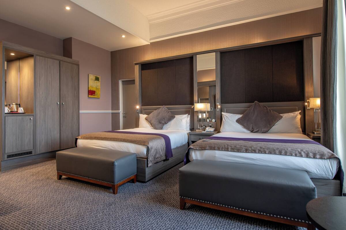 A hotel room with two beds, a wardrobe, a desk, and a mirror.