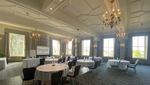 Une salle de conférence dotée de plusieurs tables et chaises, de grandes fenêtres et de lustres.