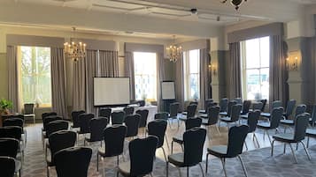 A conference room with rows of chairs, a projector screen, and a large window with curtains.