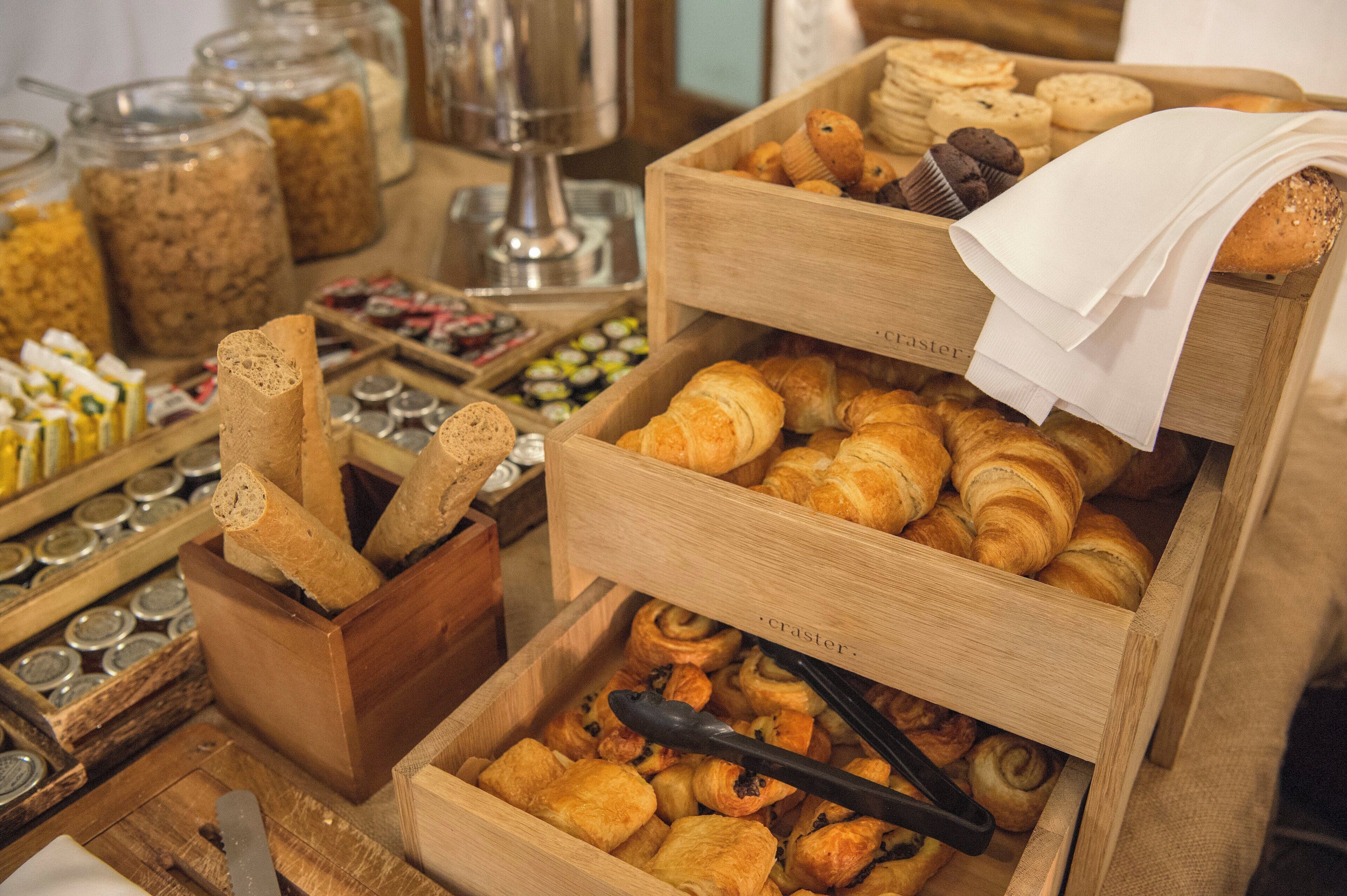 Variedad de productos horneados expuestos en recipientes de madera, como pan, pasteles y galletas.
