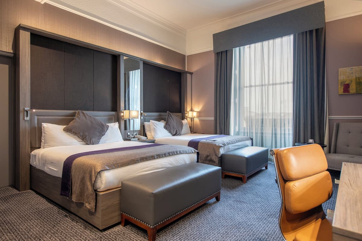 A hotel room with two beds, a sofa, a chair, and a large window with curtains.