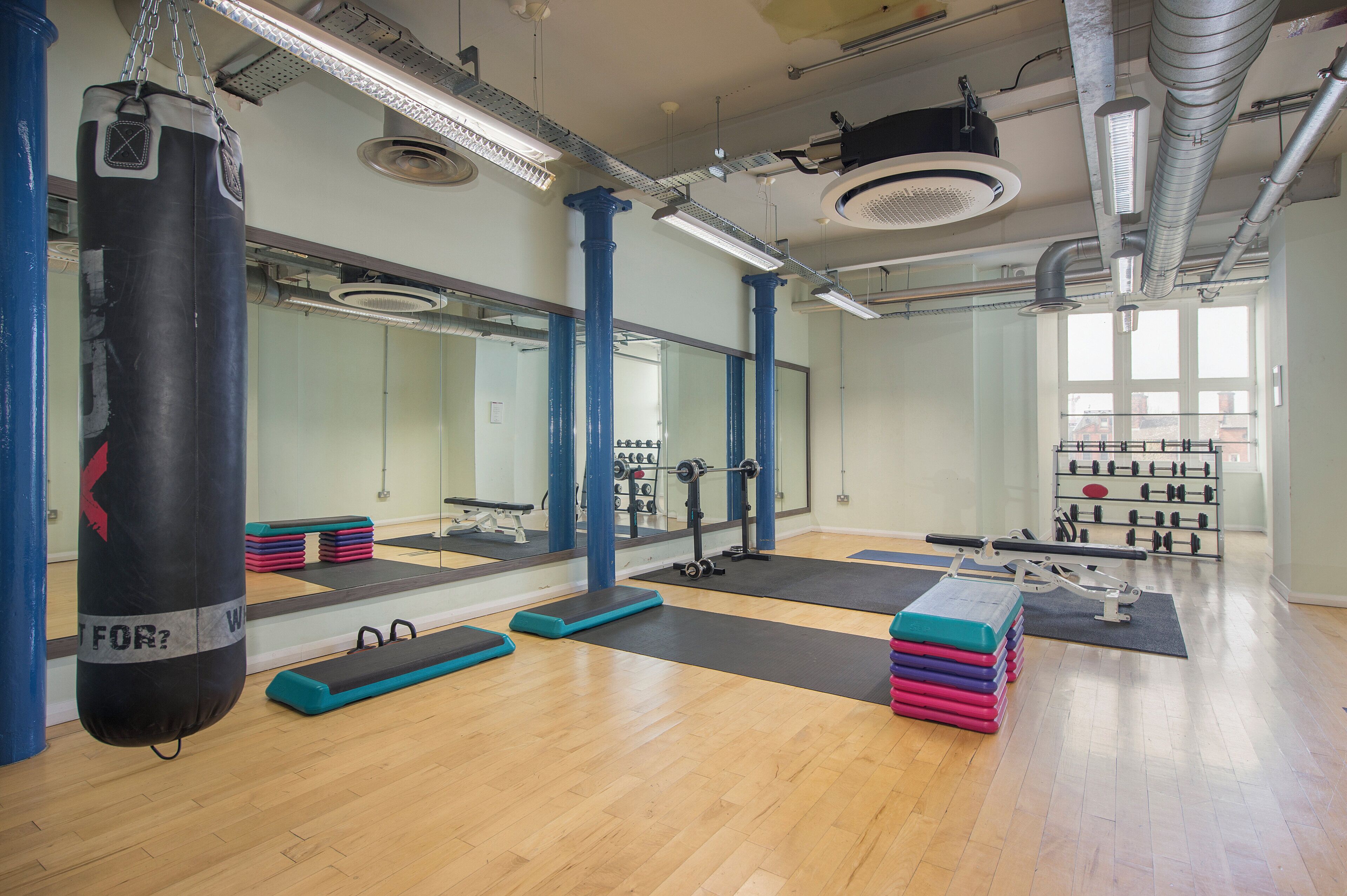 Une salle de sport équipée de matériel d’exercice, de miroirs et d’un sac de frappe.