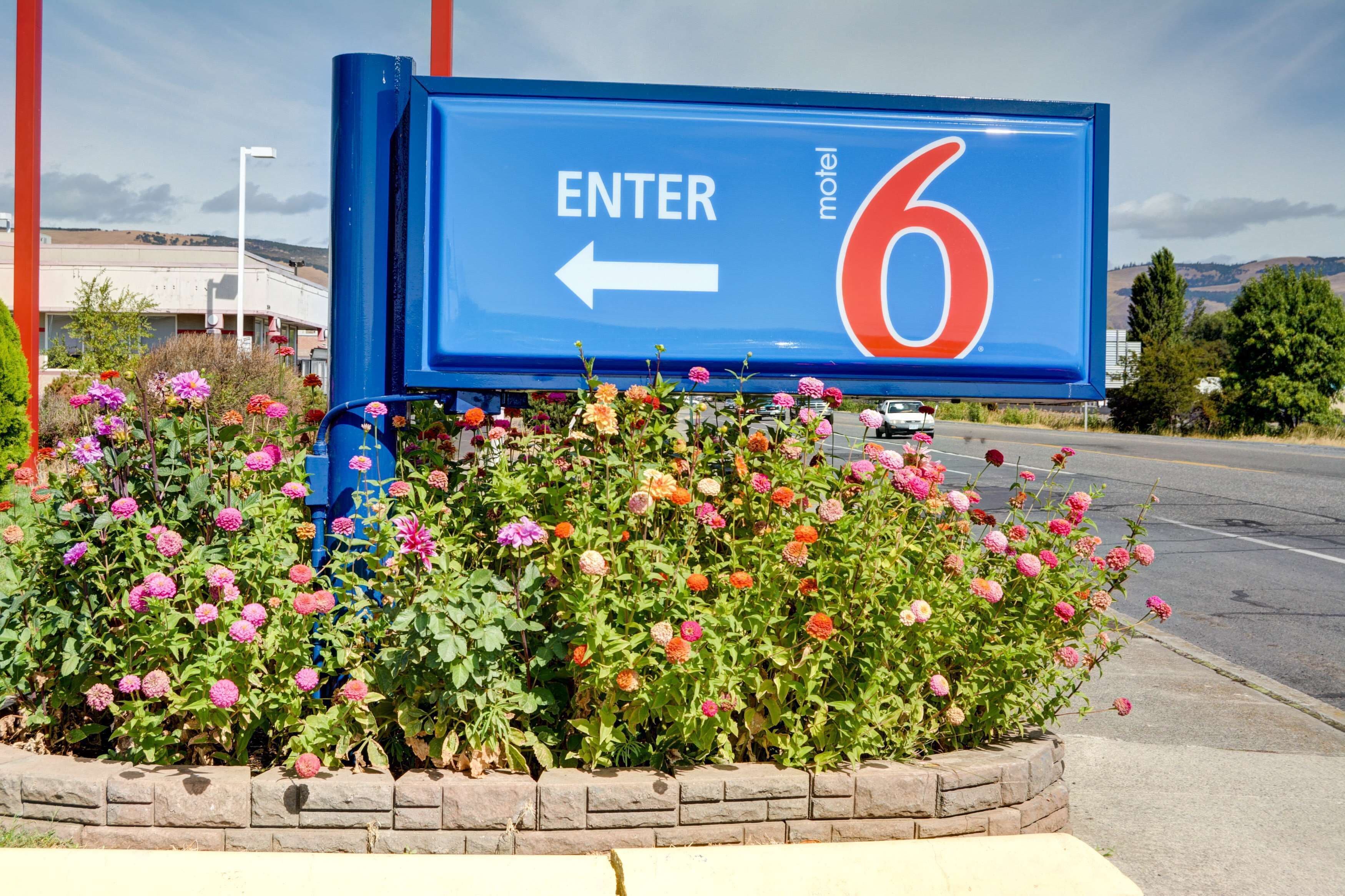 A motel sign with an arrow pointing left, surrounded by a flower bed.