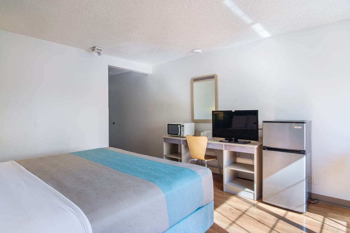 Une chambre d’hôtel équipée d’un lit, d’un bureau avec un ordinateur, d’un réfrigérateur et d’un four à micro-ondes.