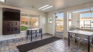 A hotel room with a large window, a flat-screen TV mounted on the wall, a dining area with a table and chairs, and a tiled floor. - Motel 6 The Dalles, OR (The Dalles)