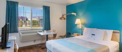 A hotel room with a bed, desk, chair, and a window with curtains.